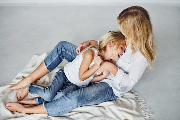 Mother with her daughter together is on the ground in the studio with white background.