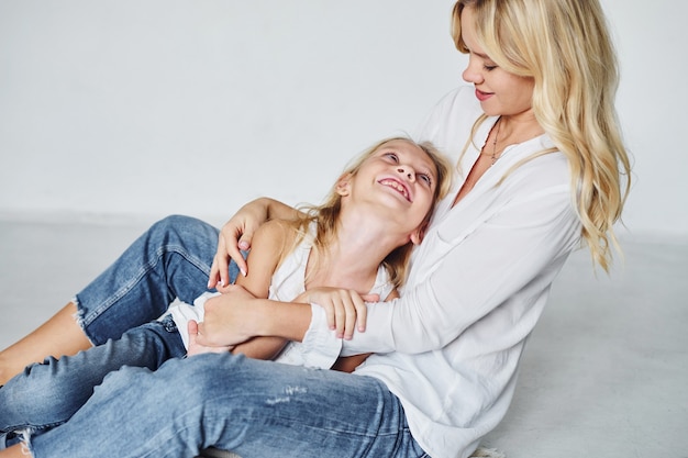 Mother with her daughter together is on the ground in the studio with white background.