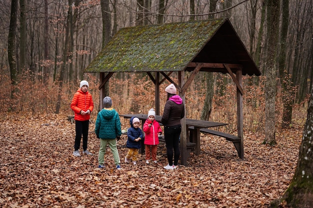 Mother with her kids having rest in autumn forest with roof shelter and picnic table