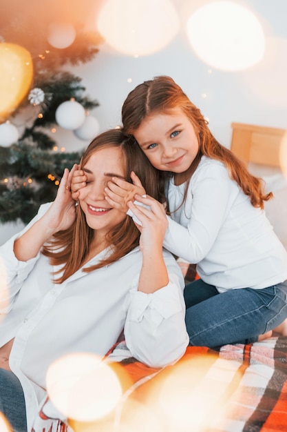 Mother with her little daughter is having fun indoors on the bed