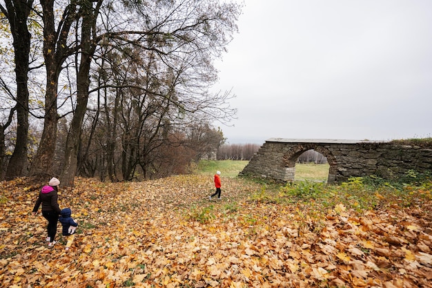 Mother with kids walking in autumn leaves near old stone arch