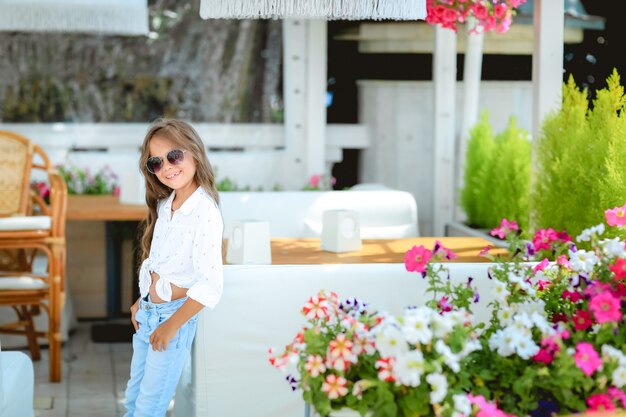 Photo mother with little charming daughter are sitting in the summer terrace in sunlight. they are have brunch. focus on the girl. real emotions. the girl is looking at camera. beautiful portrait.