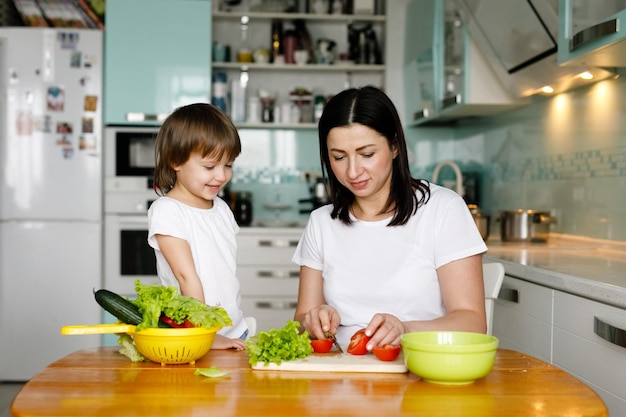 Mother with little smiling daughter cooking together in the kitchen at home