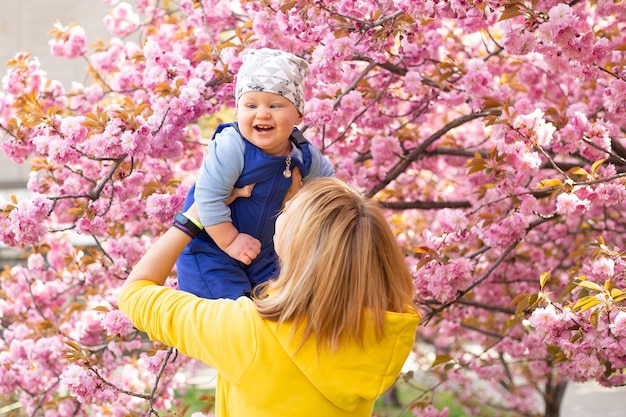 Mother with little son in the park playing near the sakura tree