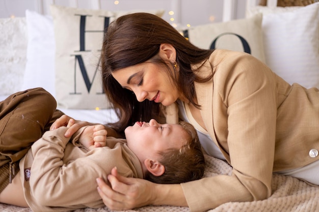 A mother with a small baby boy play hug and kiss at home on a bed in natural brown tones a happy family with a small child has fun together