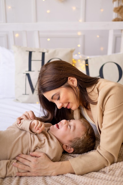 A mother with a small baby boy play hug and kiss at home on a bed in natural brown tones a happy family with a small child has fun together