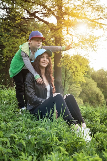 Mother with son having fun on green lawn evening in summer public park together on sunset