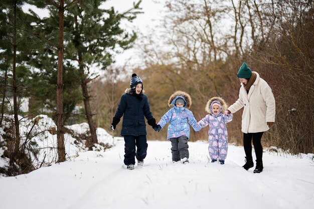 Mother with three kids holding hands and walking in winter forest