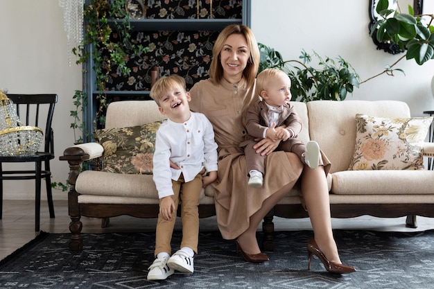 Mother with two small children in a cozy atmosphere sit on the sofa and look at the camera