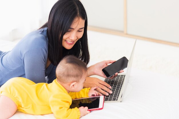 mother work from home busy on laptop computer and his baby daughter playing smartphone