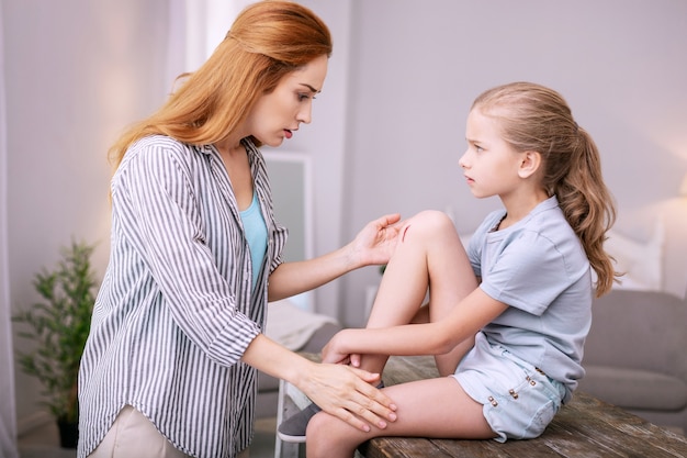 Mothers concern. Nice worried mother looking at the daughters knee while being shocked