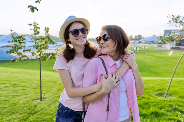 Mothers day, happy smiling hugging mother and teenager daughter. Outdoor green lawn sunset background