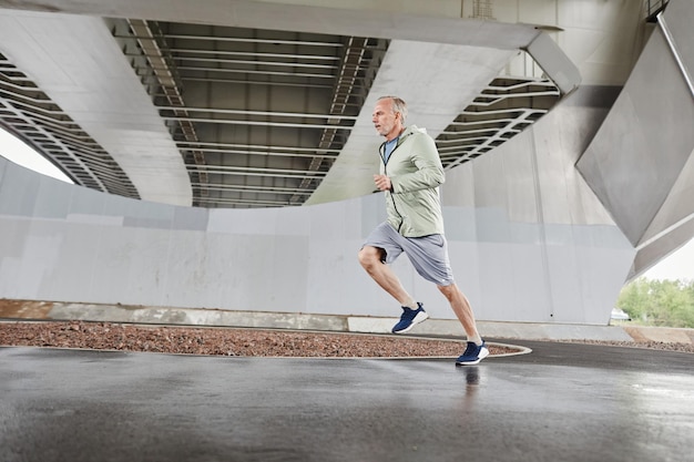 Motion shot of active mature man running against concrete background in urban city setting copy spac