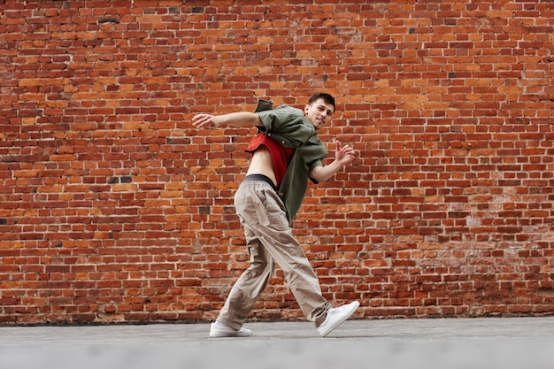 Motion shot of young man dancing hiphop style outdoors against brick wall copy space