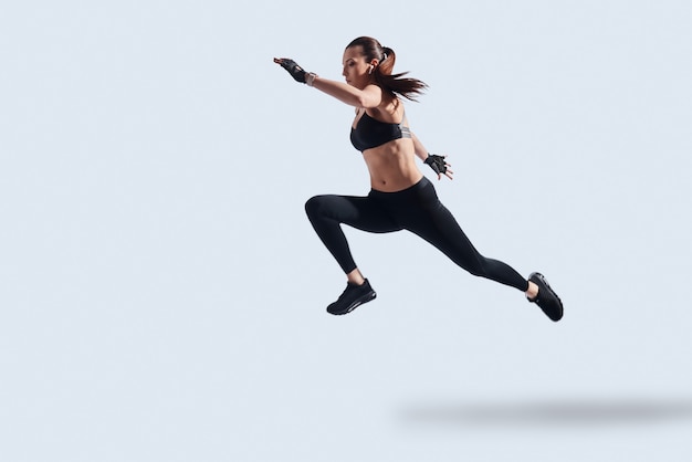 Motivated to shape her body. Full length of attractive young woman in sports clothing exercising while hovering against grey background