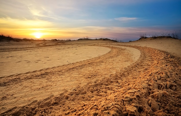 Motocross and auto sport track with sunset sky background. Wheel tracks on sand