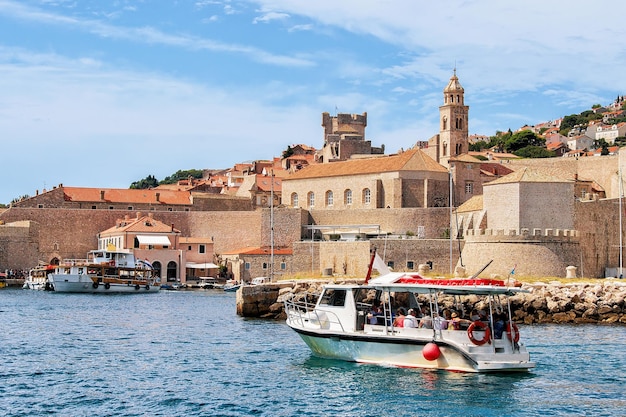 Motor boat with people at the Old port in the Adriatic Sea of Dubrovnik, Croatia. Dominican Monastery steeple on the background