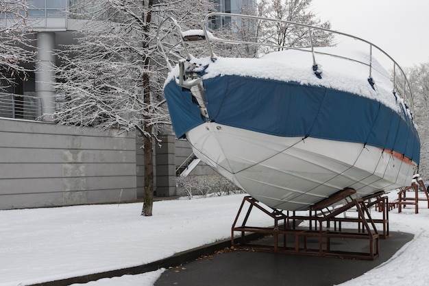 The motorboat is covered with a cover and stands outdoors in the snow Preparing the boat for winter