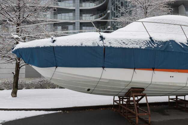 The motorboat is covered with a cover and stands outdoors in the snow Preparing the boat for winter