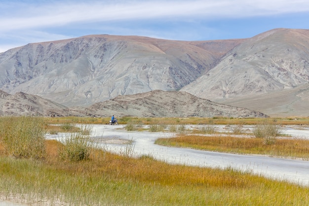 A motorcyclist takes a motorcycle through a white mountain river, his friend helps him. Mongolia, Altai.