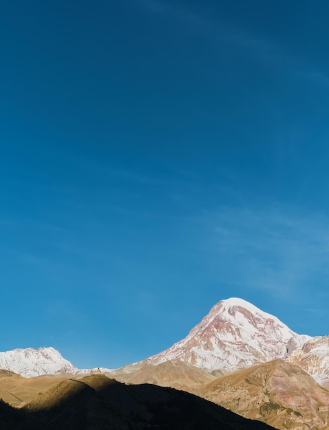 Mount Kazbek in the rays of the morning sun vertical frame early autumn in the mountains High Caucasus Georgia