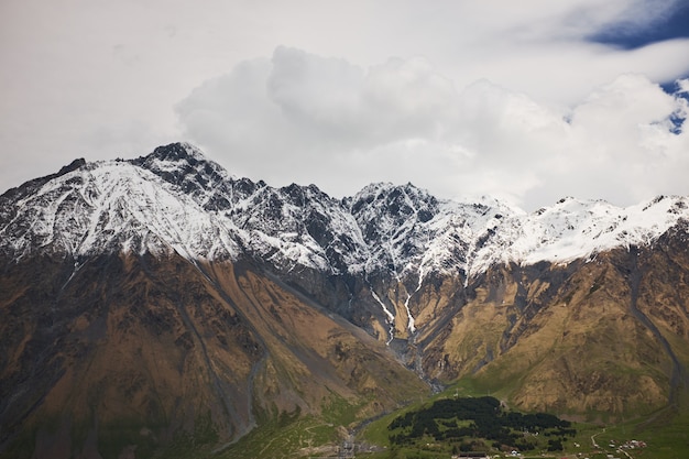 Mountain autumn landscape with high snowy peaks and blue sky with clouds