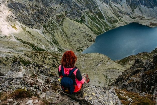 Mountain lake picturesque scenery. High rocks. Beautiful landscape. Travelling woman sitting on the mountain top.