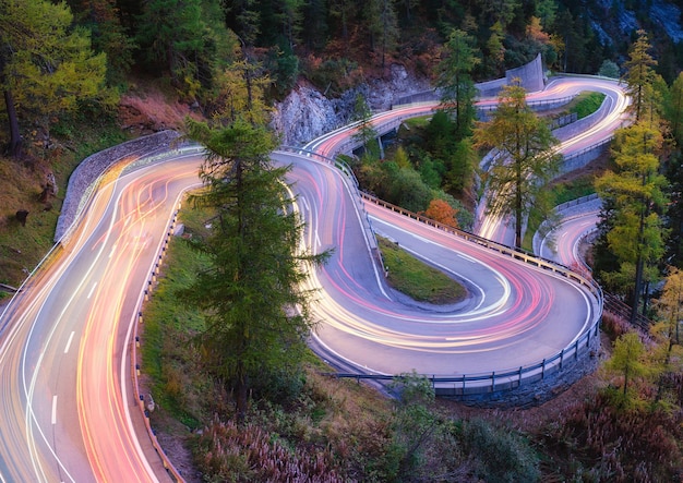 The mountain pass of Maloja Switzerland A road with many curves among the forest A blur of car lights Landscape in evening time Large resolution photo for design