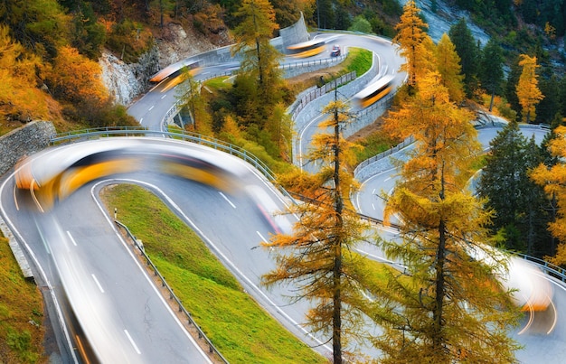 The mountain pass of Maloja Switzerland A road with many curves among the forest Blurred lights of a bus Landscape in autumn time Large resolution photo for design