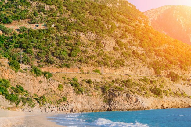 Mountain road with trees and blue waves of the sea at sunset