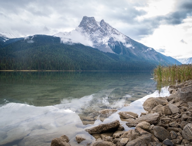 Mountain shrouded with clouds reflected in still waters of greenish lake