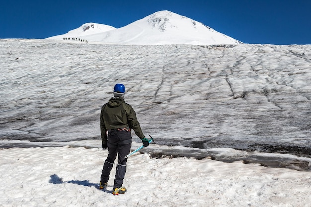 Mountaineer man in crampons and helmet with ice axe looking to Elbrus mountains summits. Group of mountaineers on a background. Active lifestyle, freedom, success concept.