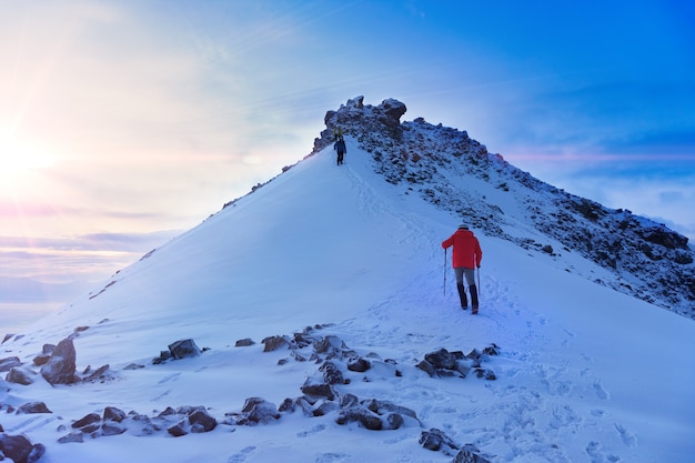 Mountaineer reaches the top of a snowy mountain in a sunny winter day