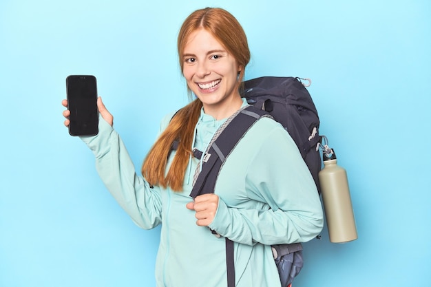 Mountaineer redhead with phone and backpack in blue studio