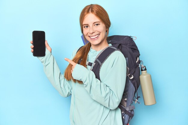 Mountaineer redhead with phone and backpack in blue studio