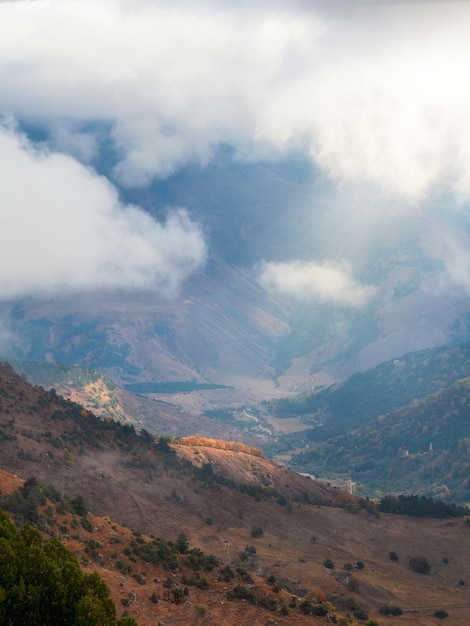 Mountains in a dense fog and sunny slope Mystical landscape with beautiful sharp rocks in low clouds Beautiful mountain foggy scenery on abyss edge with sharp stones Vertical view