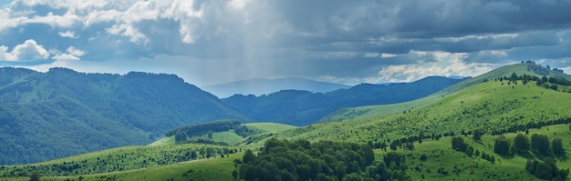 Mountains and hills in stormy weather contrasting light summer greenery of forests and meadows panoramic