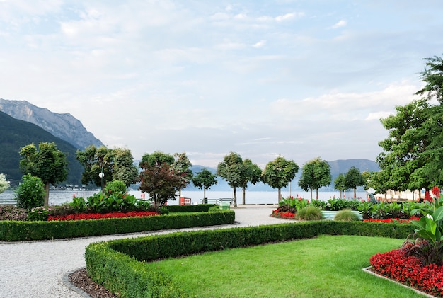 the mountains, the lake and the embankment of the city with trimmed trees, shrubs, lawn and flower beds.