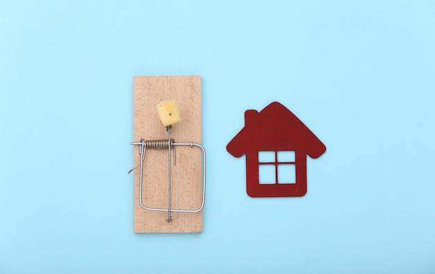 Mousetrap with cheese and house on blue background. The home buying trap