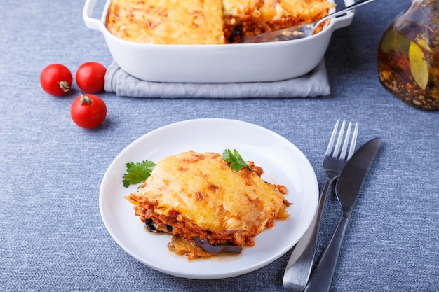 Moussaka with meat eggplant tomatoes potatoes bechamel sauce and cheese on a white plate Traditional Greek dish Closeup