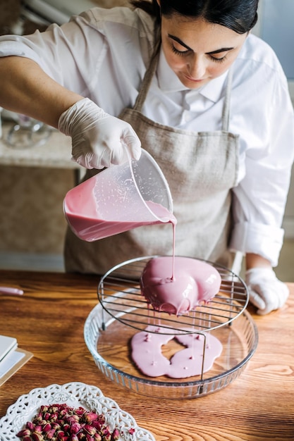 Mousse heart shape pink cake in hand of asian arabic woman pastry chef mirror glaze cake process