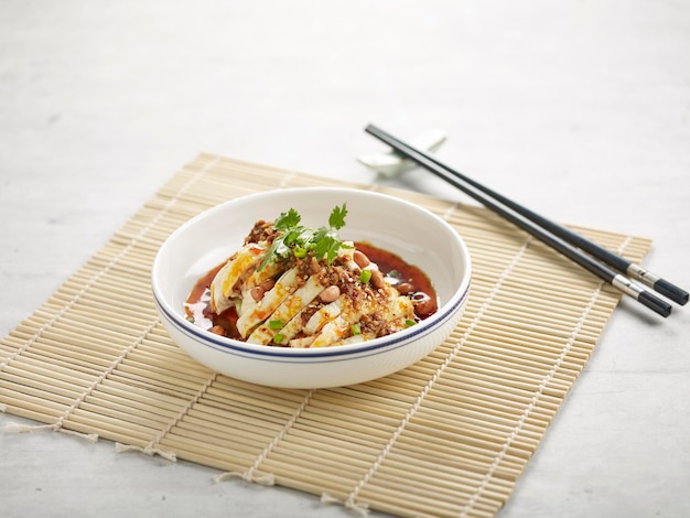 Mouth Watering Chicken slice with sauce and chopsticks in a dish isolated on wooden mat side view on grey background