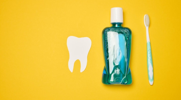 Mouthwash and toothbrush on yellow background top view