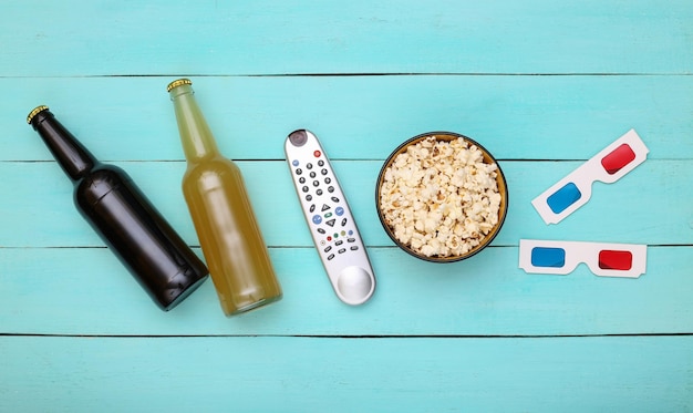 Photo movie time. beer bottle, tv remote, 3d glasses and popcorn bowl on blue wooden background. top view