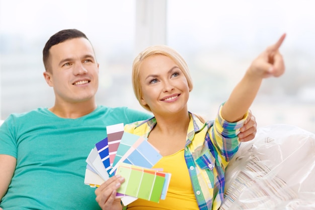 moving, home and couple concept - smiling couple looking at color samples in new home