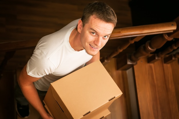 Moving house. Young man with cardboard boxes on a stairs.