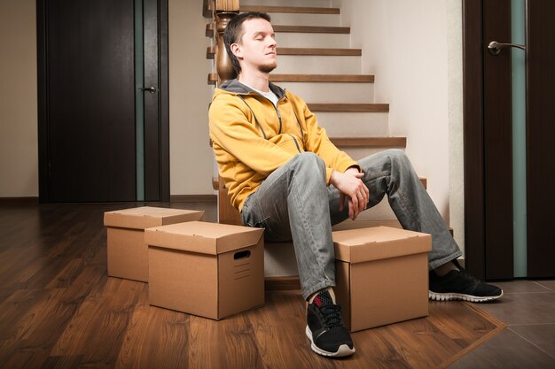 Moving house. Young man with cardboard boxes on a stairs.