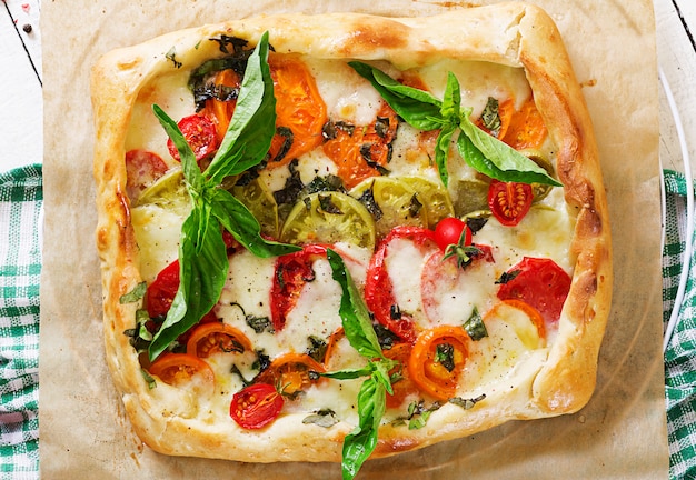 Mozzarella, tomatoes, basil savory pie on a white wooden table. Delicious food, appetizer in a mediterranean style. Top view. Flat lay