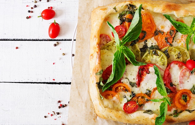 Mozzarella, tomatoes, basil savory pie on a white wooden table. Delicious food, appetizer in a mediterranean style. Top view. Flat lay