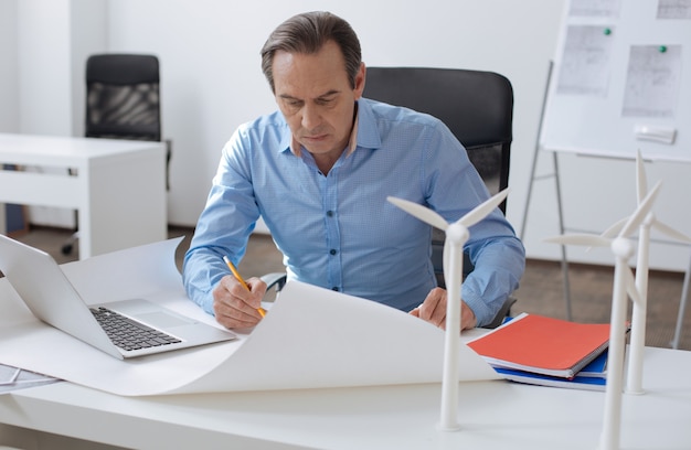 Much work to do. Concentrated professional engineer sitting at the table and drawing the scheme while working on the project